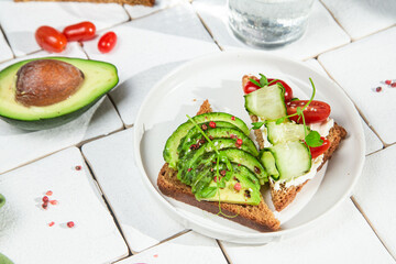 Toast with cream cheese, avocado, cucumber and tomato on a table