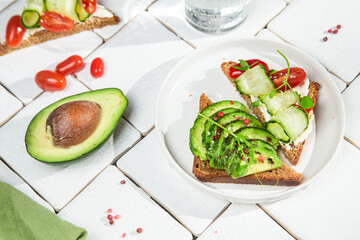 Toast with cream cheese, avocado, cucumber and tomato on a table