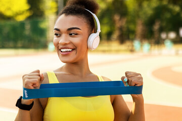 Smiling African Woman In Headphones Exercising With Elastic Band