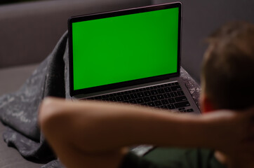 Caucasian man uses laptop with greenscreen of chromakey mockup. Person watches the video, relaxes, enjoys the rest on personal computer. Green screen and chroma key.