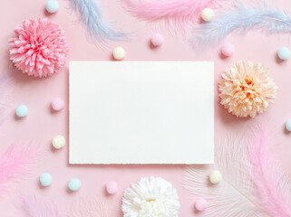 Blank card between pastel flowers, pom-poms and feathers near ring in a gift box on pink