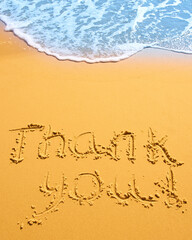 Thank you written in the sand on the beach.