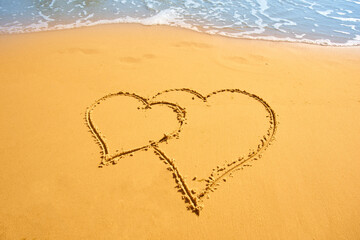 Two hearts handwritten on sand of tropical beach