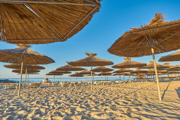 Seashore, sand beach with umbrellas and sunbeds on background of the sea and sky