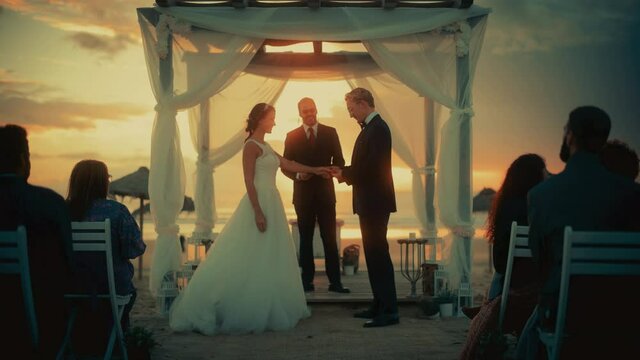 Beautiful Bride and Groom During an Outdoors Wedding Ceremony on an Ocean Beach at Sunset. Perfect Venue for Romantic Couple to Get Married, Exchange Rings, Kiss and Share Celebrations with Friends.