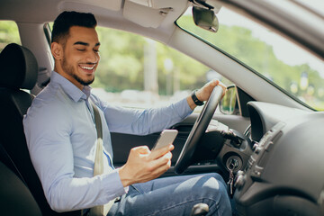Cheerful arab man using cellphone while driving car