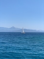 Naklejka premium Yacht with a white sail in the open sea. A sailboat sails in the ocean off the coast. Boat with a sail on the waves of a calm sea.