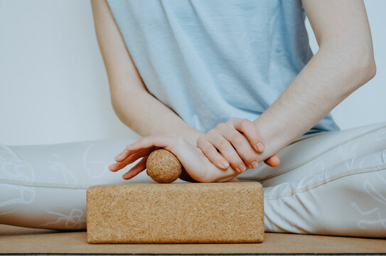Front view close up of person doing palmar fascia release with a small cork ball on a cork block. Concept: self care practices at home, SMFR, sustainable, eco friendly props