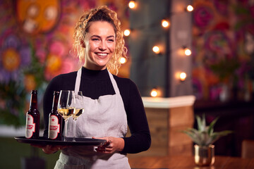 Portrait Of Smiling Female Server Holding Tray Of Drinks In Cool Bar Or Club