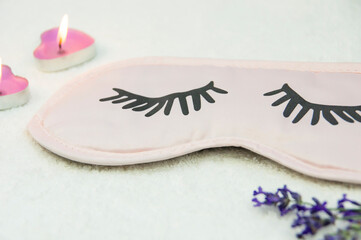 Sleep mask with natural lavender and candles on white bedding. Side view, close-up.