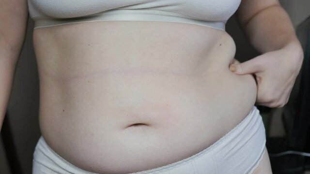 a woman shows excess weight on her stomach and sides and is nervous with a sharp gesture of her hands. Takes his layer of fat with his hands and crushes it
