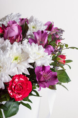 Floral arrangement in hat box on light background. Bouquet with red roses, white chrysanthemums and lilac alstroemeria
