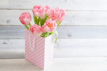 Beautiful bouquet of fresh real tulips stands in gift bag in pink dot, white boards background. Happy birthday, gift, mother's day, valentine, 8 march, spring shopping, springtime concept.  Copy space