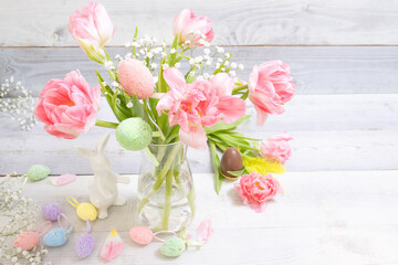 Beautiful pink tulips, decorative Easter eggs, Bunny, chocolate egg on background of white boards. Concept of stylish Easter decor, tradition of hiding eggs, spring time, festive mood. Horizontal.