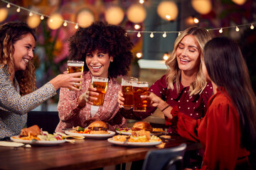 Multi-Cultural Group Of Female Friends Enjoying Night Out Eating Meal And Drinking In Restaurant