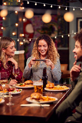 Multi-Cultural Group Of Friends Enjoying Night Out Taking Picture Of Food On Mobile Phone