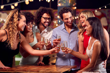 Multi-Cultural Group Of Friends Enjoying Night Out Drinking In Bar Together Making A Toast