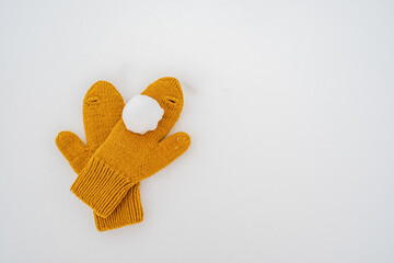 Snowball on yellow knitted mittens, in the snow. Winter active games and entertainment. Copy space. 