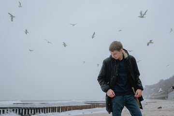 the young man stands with his eyes down, seagulls fly over the sea in the sky