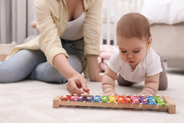 Cute baby and mother playing with xylophone on floor at home