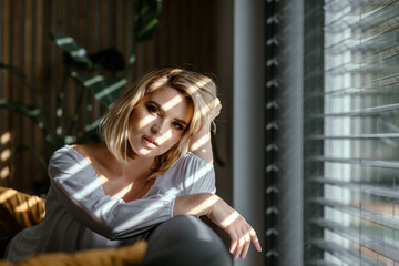 Fototapeta na wymiar Glamour portrait beautiful lady at home looking through the window with sun beams on face