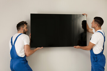 Professional technicians installing modern flat screen TV on wall indoors - obrazy, fototapety, plakaty