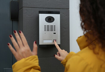 African-American woman ringing intercom while waving to camera near building entrance