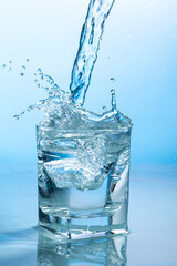 Naklejka na ściany i meble splash of water in a transparent glass on a blue background
