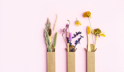 Zero wast multicolored bamboo toothbrushes with dried flowers, on pink background. Wooden personal dental care accessories. Plastic free, eco friendly, sustainable lifestyle concept