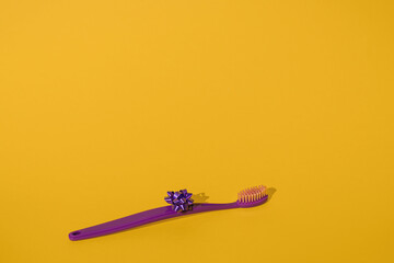 Single new isolated purple toothbrush with a ribbon bow on a bright vibrant yellow background with copy space. Minimal dental theme. Orthodontist medical mockup. Fun hygiene for kids. Very peri.