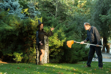 A young beautiful girl in a witch's costume is trying to bewitch a man who is holding a garden...