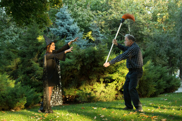 A young beautiful girl in a witch's costume is trying to bewitch a man who is holding a garden...