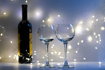 Two transparent empty glasses, a bottle of wine and a bokeh from the lights. The eve of a romantic dinner. A postcard for holidays and dinners.