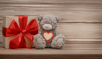 Teddy bear holding a gift on wooden background