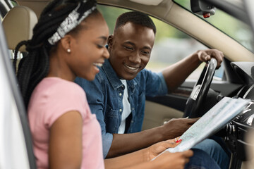 Happy black woman showing her boyfriend map, sitting in car