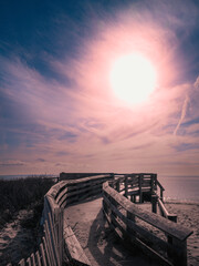 The white sun glowing with a soft pink ring on the blue cloudy sky background over the wooden beach deck