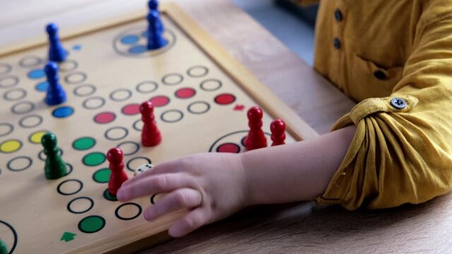 close-up of hands of small child manipulate with wooden figurines of family board game, smart kid, 2-year-old girl is learning to count, Cross and circle game Parcheesi, foreground focus