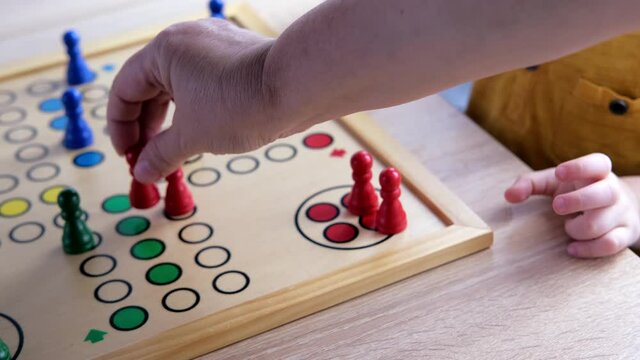 close-up of hands of small child manipulate with wooden figurines of family board game, smart kid, 2-year-old girl is learning to count, Cross and circle game Parcheesi, foreground focus
