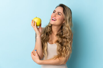 Young Brazilian woman isolated on blue background with an apple and happy