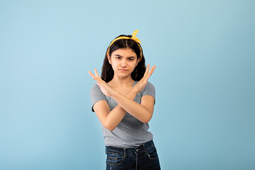 Indian teenage girl gesturing STOP, crossing hands near chest on blue studio background