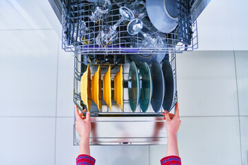 Open dishwasher with shiny clean dishes in a white home kitchen