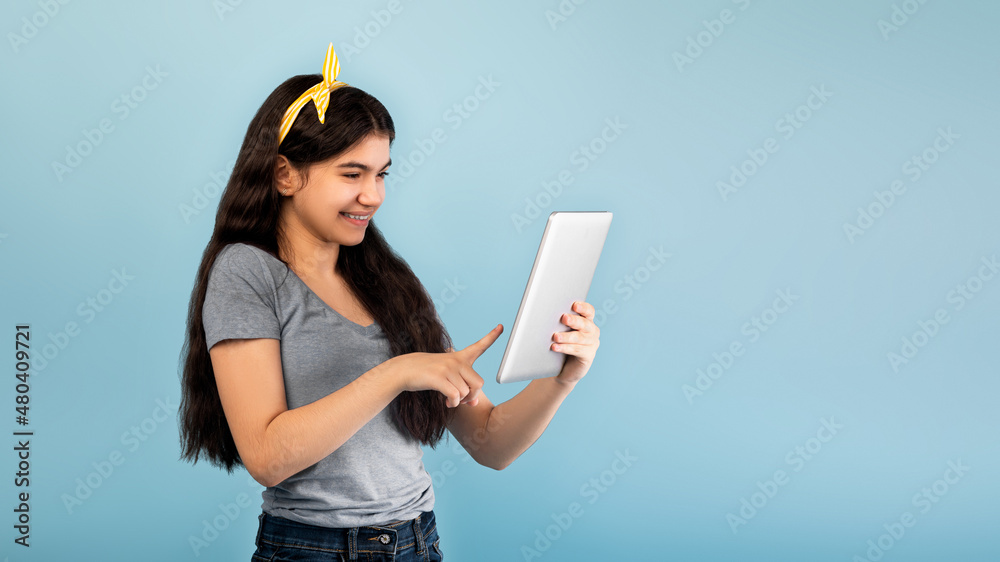 Wall mural portrait of indian teen girl using tablet computer, studying online on blue studio background, panor