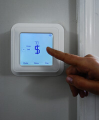 Finger pointing to a dollar sign on a smart thermostat -- heating and cooling cost concept - 480411131
