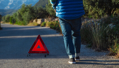 Man with his back to the camera puts a warning triangle behind his car