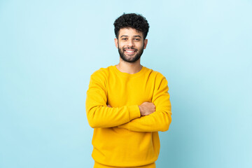 Young Moroccan man isolated on blue background keeping the arms crossed in frontal position