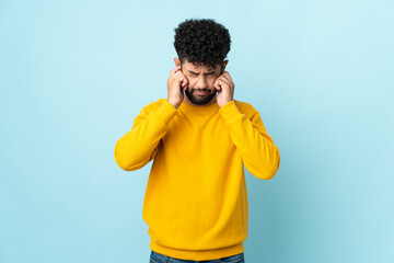 Young Moroccan man isolated on blue background frustrated and covering ears