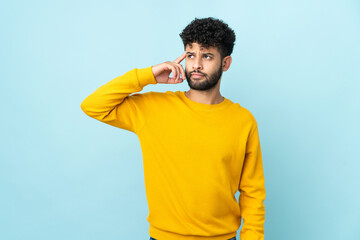 Young Moroccan man isolated on blue background making the gesture of madness putting finger on the...