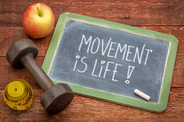 movement is life inspirational message -  white chalk text on a slate blackboard sign with a dumbbell, apple and tape measure, fitness and lifestyle concept