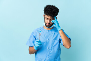 Moroccan dentist man holding tools isolated on blue background with headache