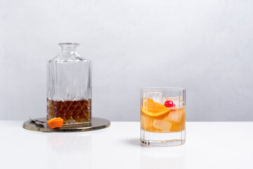 Vaso de vermut con hielo decorado con cerezas, rodajas de naranja y decantador sobre mesa blanca	